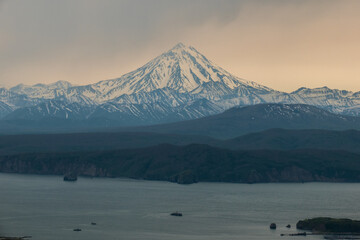 Panorama of the Avacha Bay with two ships on water and coast with hills covered by forest and volcano Vilyuchik also known as Vilyuchinsky with cloud hat at bad weather. Kamchatka Peninsula, Russia