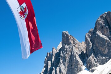 Die Flagge Südtirols weht  vor einem strahlend blauen Himmel und den imposanten Geislerspitzen in...