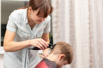 young mom hairdresser cuts her baby boy at home with hair clipper during quarantine. selective focus. portrait