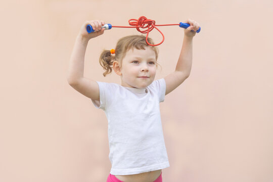 Little Caucasian child girl of five years old, curly blonde girl with a rope in her hands. Children's sports concept.