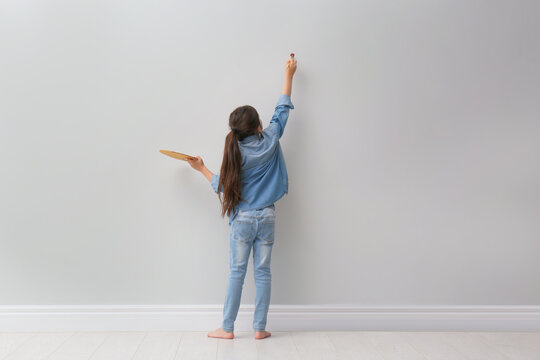 Little girl painting on light grey wall indoors, back view. Space for text