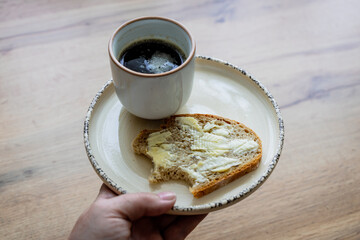 Weibliche Hand hält einen Teller mit einem Butterbrot und einer Tasse Kaffee. Servieren,...
