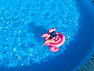 Summer holidays, relaxation. Woman on flamingo pool float in pool, drone aerial view. Enjoying summer vacations during quarantine.
