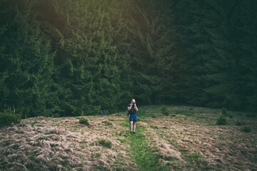 Naklejka premium A handsome young hipster man walking in the mountains. Hiker photographs nature against the background of a dark forest.