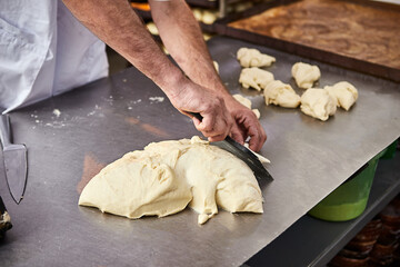 Bakers hands form dough for baking bread and put it into oven-tray at the manufacturing