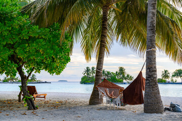 A man relaxing in a hammock under palm trees on a tropical island in the evening