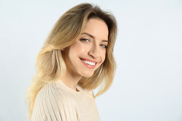 Fototapeta premium Portrait of happy young woman with beautiful blonde hair and charming smile on light background. Space for text