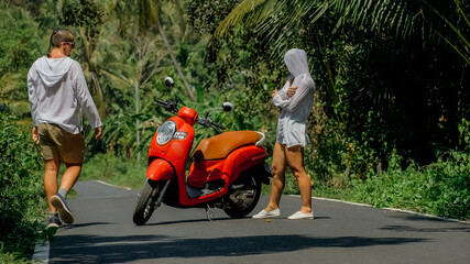 Two caucasian tourist woman man dance near scooter. Love couple on red motorbike in white clothes, sunglasses on forest road trail trip. Dancing road. Motorcycle rent. Asia Thailand ride tourism.