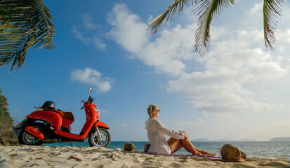 Scooter road trip. Woman alone on red motorbike in white clothes on sand beach by ocean. One girl...