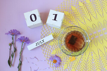 Calendar for July 1 : cubes with the numbers 0 and 1, the name of the month of July in English , a cup of tea on a yellow openwork napkin, flowers on a pastel background
