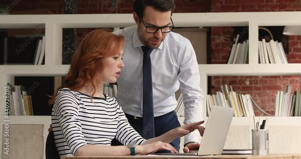 Canvas Prints Smart young male team leader in glasses instructing millennial red-haired intern, helping with corporate computer software application on computer, reviewing work or discussing online project.