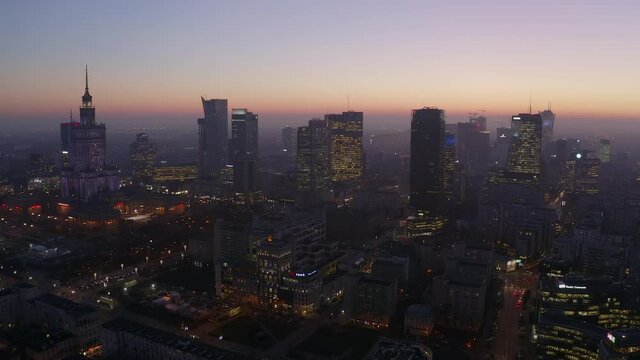 Drone view of the beautiful urban metropolis with skyscrapers and orange sky after sunset in the business center of Warsaw, Poland. The camera descends on a night city with night traffic and skyscrape