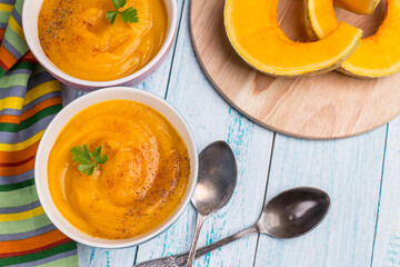 Traditional autumn pumpkin soup with bright masks on a blue background. Vegetarian delicious food.