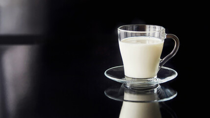 Milk in a transparent glass cup on a black background.