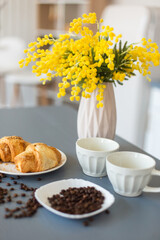 Coffee, croissants and yellow flowers in vase in the kitchen. Breakfast, home, coffee time concept