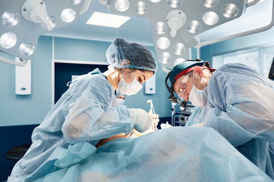 Surgeons in a light operating room perform plastic surgery, a team of male and female doctors perform reconstructive surgery