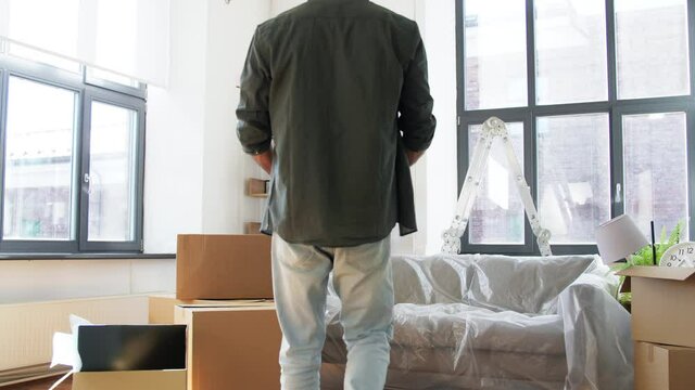 moving, people and real estate concept - happy smiling man with boxes sitting on sofa covered with plastic sheeting at new home