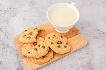 Close up of cereals cookies are stacked on cutting board, cookies topped with almonds, raisins, sunflower seeds, pumpkin seeds, whole grains.