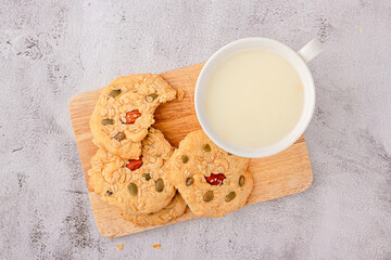 Top view of cereals cookies are stacked on cutting board, cookies topped with almonds, raisins, sunflower seeds, pumpkin seeds, whole grains.
