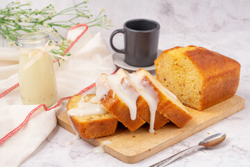 Sliced pound cake topped with lemon glaze on a cutting board and spoon are marble table.
