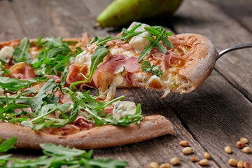Slice of pizza with cured ham, blue cheese, pear, pine nuts, arugula