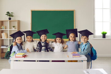Portrait of a group of cute little graduates of kindergarten or junior class in bachelor hat or mortarboard. Concept of childhood, school, education, knowledge, graduation and people. - obrazy, fototapety, plakaty