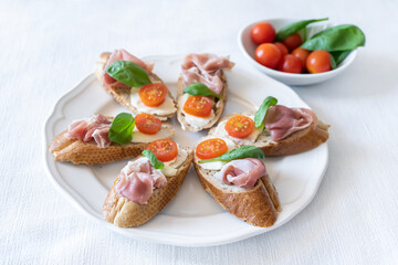 Bruschettas with prosciutto, mozzarella and cherry tomatoes on a white plate, closeup. Italian style cuisine.