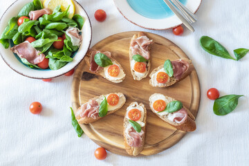 Bruschettas with prosciutto, mozzarella and cherry tomatoes on a wooden board, closeup. Italian style cuisine.