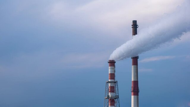 4k timelapse footage of two stacks of combined heat and power station against dark blue sky and clouds. White smoke swings on one stack in the wind.
