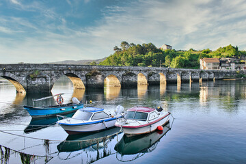 Barca y lanchas de pescador junto al puente medieval sobre el río Verdugo en Pontesampaio,...