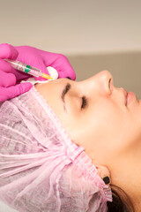 Young woman receiving an injection of anti-aging botox filler to the forehead from a cosmetologist in a beauty salon. Facial treatment injection