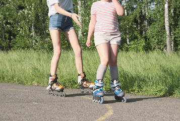 teenager girl and her little sister rollerskating in the park. partial view. sport and leisure concept. preshcool girl and teen spending time together