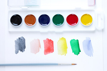 A set of watercolor paints, a paint brush and watercolor color blurs colors on a white background...