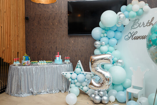 Arch of blue balloons for boy happy birthday party. Number 5 and 1 for two brothers. Festive decorative elements, photo zone with star, candy bar with two cakes and sweets. Inscription Nilita.