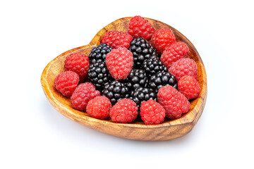 Raspberry and blackberry in wooden bowl in the shape of heart isolated on white background.