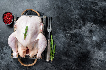 Farm Raw whole chicken in a wooden tray. Black background. Top view. Copy space