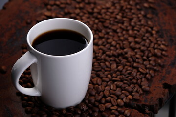 black coffee in white mug with surrounded by roasted coffee beans on dark red wood table