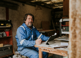 Senior carpenter writing on his notebook with laptop on the desk small business concept..