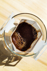 Glass cup with drip coffee bag on wooden table closeup. Instant paper macro sachet above. Fresh...