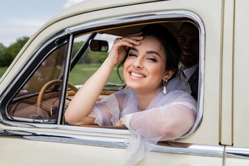 Happy bride looking at camera near window of vintage auto