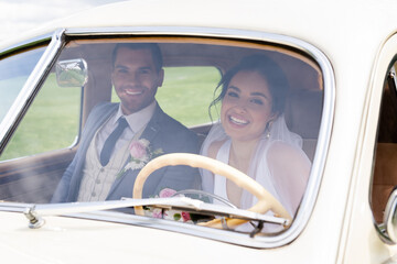 Smiling bride and groom looking at camera from retro car