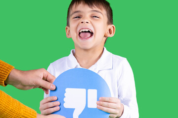 Child in white shirt is holding in his arms a paper, circle form, blue color with a sign thumb down. Green background.