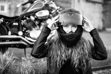 Red-haired curly woman in a helmet near a motorcycle. Monochrome.