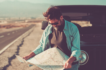 Man and travel people with car vehicle transport concept - adult male looking a paper map outside his automobile - long asphalt road in background - choosing destination