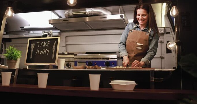 Caucasian chef woman working inside food truck at night time preparing dinner food - Summer and small business concept
