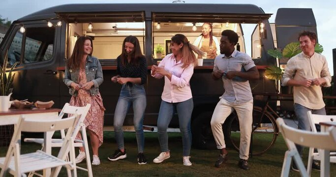 Multiracial people dancing in front of food truck outdoor - Multigeneratiol friends having fun eating dinner outside at summer time 