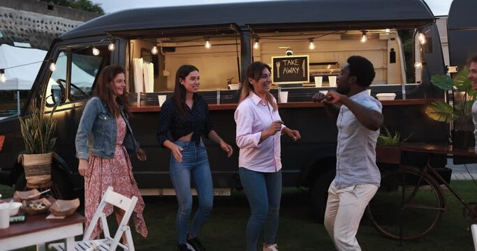 Multiracial people dancing in front of food truck outdoor - Multigeneratiol friends having fun eating dinner outside at summer time 