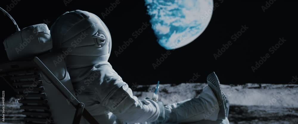 Poster back view of lunar astronaut having a beer while resting in a beach chair on moon surface, saluting 