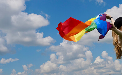 Bisexual, lesbian, woman, transgender holds LGBT flag against blue sky with clouds on a sunny day...