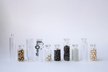 Small glass jars stand side by side in one line. Transparent containers filled with beads